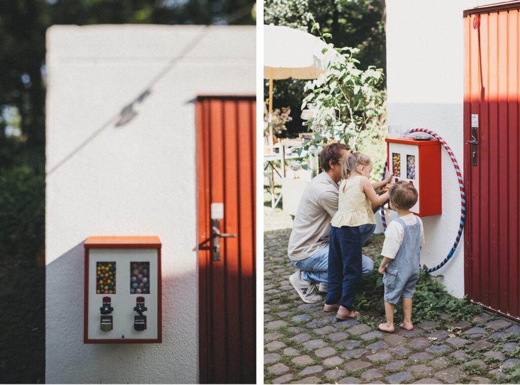 Geteiltes Bild: Links sind zwei Süßigkeitenautomaten an einer weißen Wand neben einer roten Tür zu sehen. Rechts, aufgenommen von Familien Fotograf, spielen ein Erwachsener und zwei kleine Kinder an einem sonnigen Tag im Freien mit den Automaten.