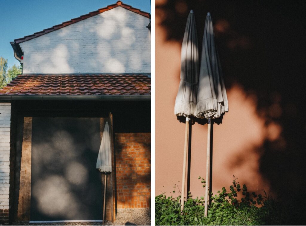 Geteiltes Bild: Die linke Seite zeigt einen geschlossenen Terrassenschirm, der einen Schatten auf eine weiße Ziegelwand unter einem Ziegeldach wirft. Die rechte Seite, von Fotografin im Fotostudio Köln, zeigt zwei geschlossene Schirme, die an einer pfirsichfarbenen Wand mit Blattschatten lehnen.