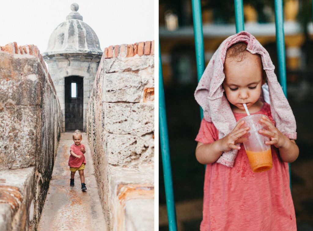 Ein kleines Kind in einem rosafarbenen Outfit sitzt auf einem Baumstamm an einem Sandstrand bei Sonnenuntergang, mit Fußabdrücken in der Nähe und dem Meer dahinter. Aufgenommen von Fotograf Köln, säumt üppiges Grün die linke Seite des Strandes und sorgt für eine perfekte Erinnerung.