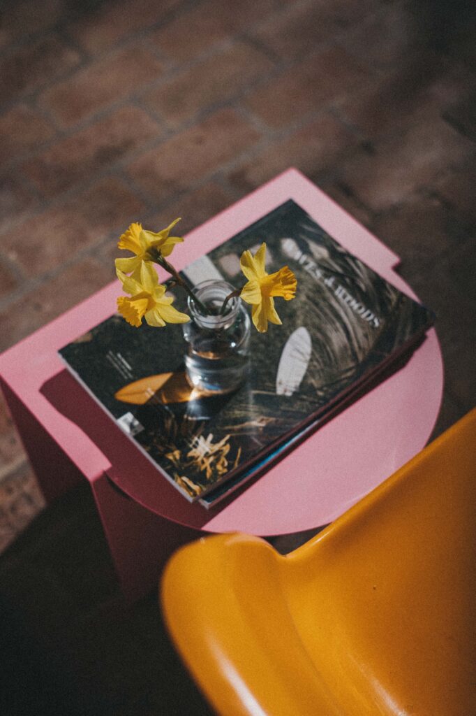 Zwei helle Räume mit weißen Backsteinwänden und Holzböden. Der linke Raum ist ideal für einen Kinderfotografen und verfügt über ein hölzernes Loft und eine Leiter, während der rechte Raum mit einem Schreibtisch, einem Stuhl, einer hohen Pflanze und einem Regal an einem hellen Fenster ausgestattet ist.